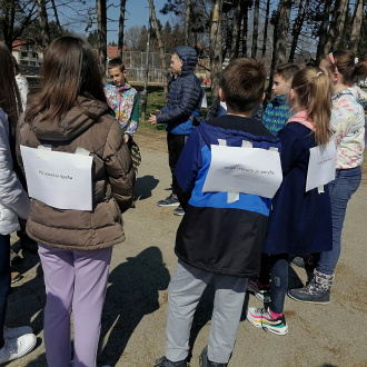 A group of students standing in a circle, they all have a4 sheets with text stuck on their backs