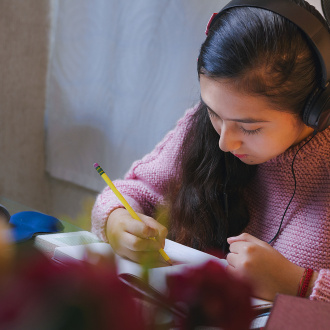 teenage girl writing in a notebook in front of a computer